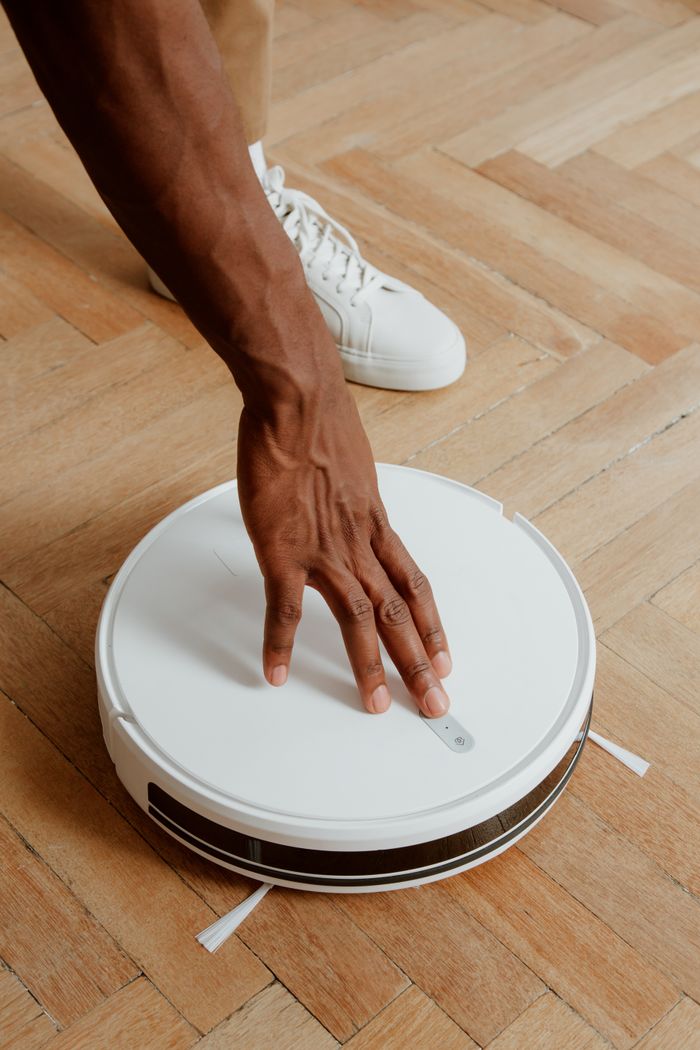 A man gently touches a robot vacuum on a parquet floor, emphasizing technology and simplicity.