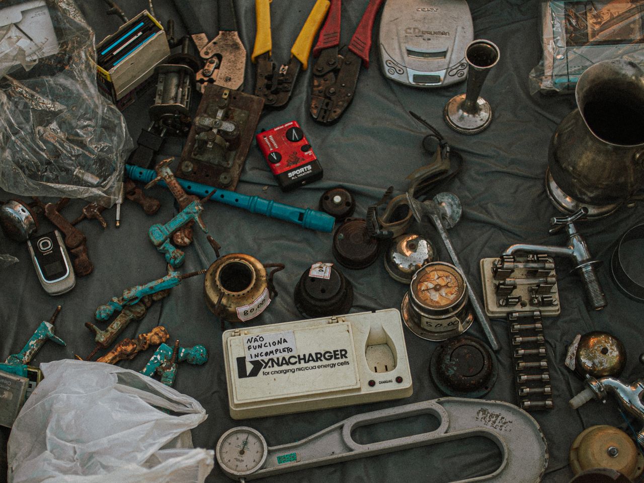 Scattered assortment of old metal tools, gadgets, and household items displayed at an outdoor flea market.