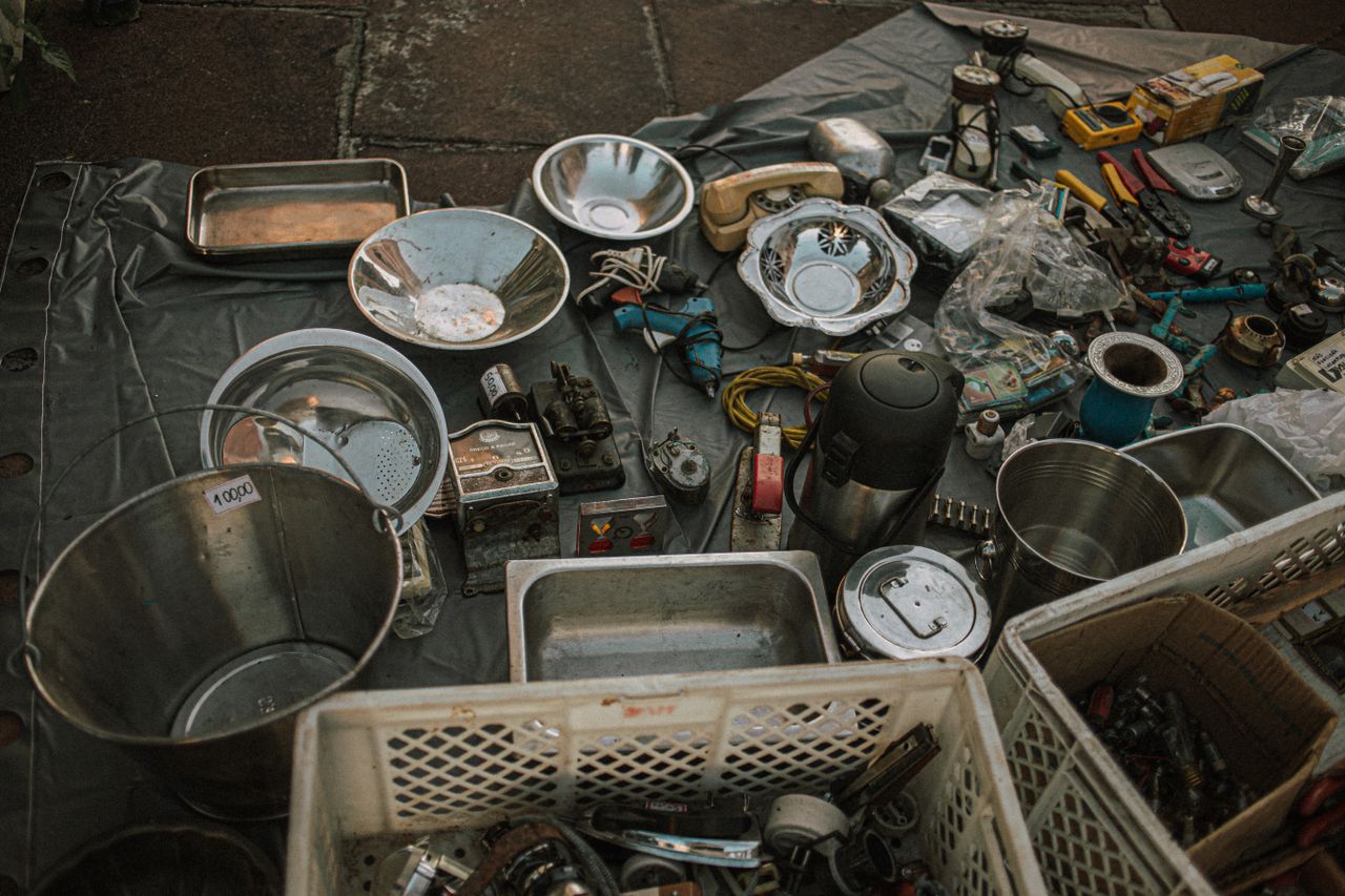 Assorted metal items and vintage tools displayed at an outdoor flea market on asphalt.